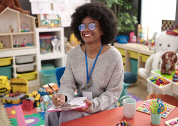 African american woman teacher smiling confident writing on document at a child care center